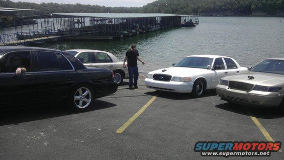 Three Ford Crown Victoria police cars parked by a lake with docks