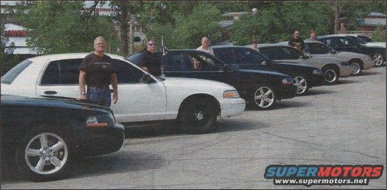 Several police interceptor sedans parked in a row, some with people standing by them