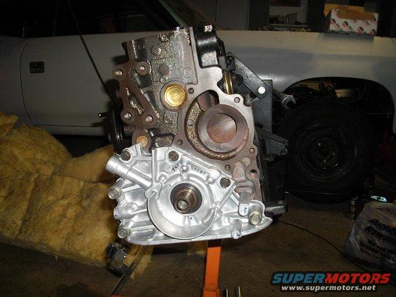 Engine block on an orange stand, with insulation to the left and a car in the background