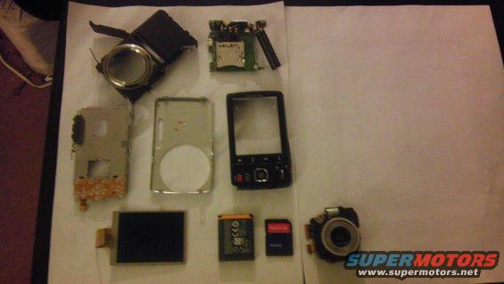 Disassembled phone parts, battery, SD card, and camera module laid out on a white surface
