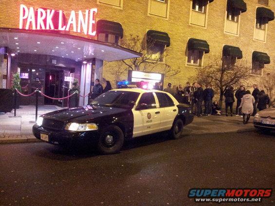 2001 Ford Crown Victoria police car parked outside Park Lane building with people gathered