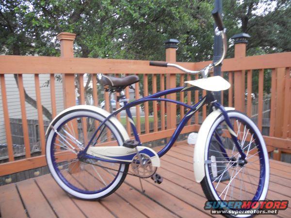 Blue and white cruiser bicycle on a wooden deck. Has whitewall tires and a brown seat