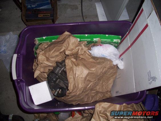 Car part wrapped in brown paper inside a purple bin with other items