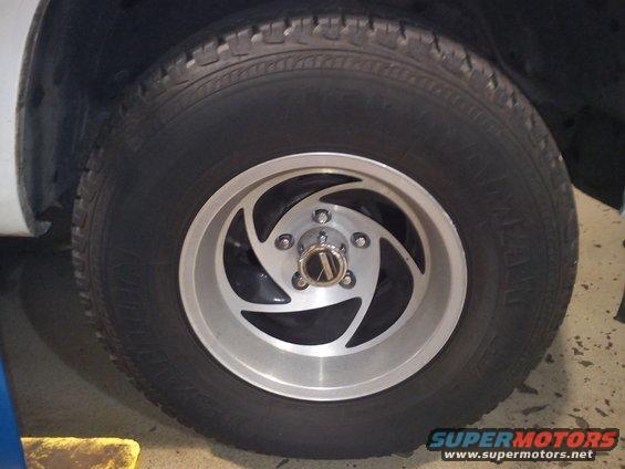 Close-up of a silver alloy wheel with a swirling spoke design and a black tire