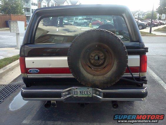 Rear view of a dark Ford Bronco with a spare tire mounted on the tailgate. It has a red and white stripe on the side and a Virginia license plate