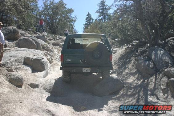 Green Ford Bronco with spare tire on rear, navigating a boulder-strewn dirt path