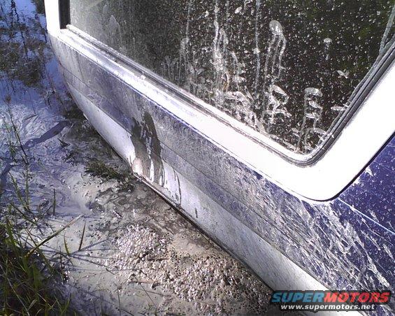 Vehicle side panel and window covered in mud, stuck in watery, muddy terrain