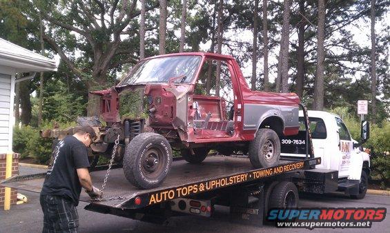 1987 Ford Bronco body being loaded onto a tow truck. A man is securing it with chains