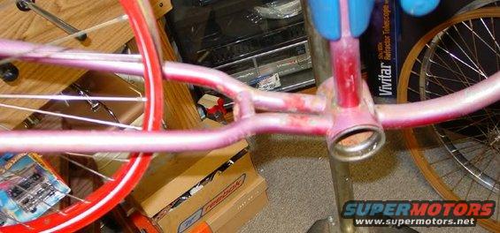 Pink bicycle frame with red accents and spokes, showing some rust