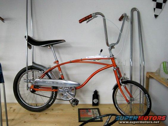 Orange bicycle with high handlebars and a banana seat, chrome fenders, and a "GTO 33" chain guard