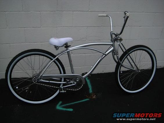 Silver bicycle with white seat and whitewall tires parked against a brick wall