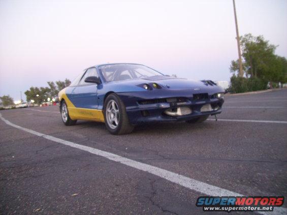 1995 Ford Probe with blue and yellow paint scheme, aftermarket front bumper, and roll cage visible through windows