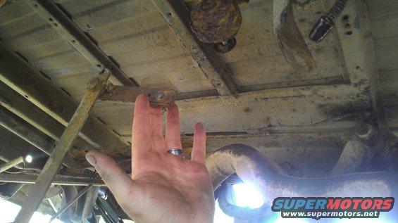 Underside truck frame with hand pointing to bracket