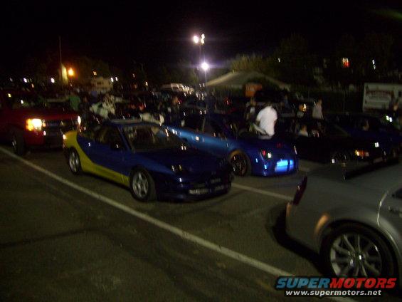 Blue and yellow sports car parked at night, other cars and people around