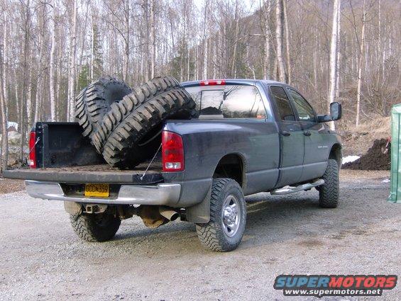 Pickup truck bed loaded with two large off-road tires. Side view