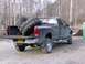 1983 Chevrolet C/K Pickup - A dark-colored pickup truck is parked outdoors with its tailgate down, carrying two oversized tires in the bed.