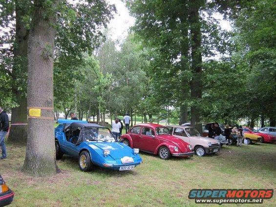 Blue custom sports car with pop-up headlights and gold wheels parked on grass