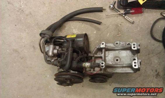 Engine component with hoses and pulleys on a concrete floor. Tools are visible in the background