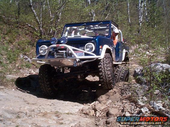 1977 Ford Bronco with custom bumper and roll cage driving on a rocky trail
