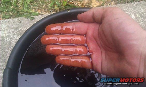 Hand with fingers in dark fluid in a black pan, Supermotors.net logo visible