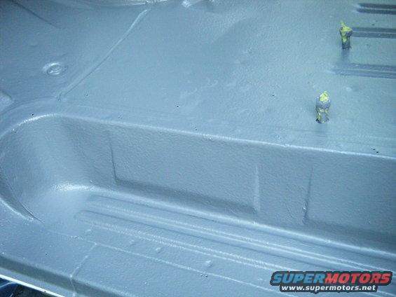 Gray painted vehicle floor with raised ribs and two yellow-capped bolts