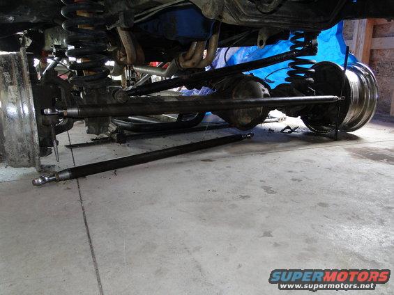 Undercarriage of a vehicle showing suspension, differential, and driveshaft components. One driveshaft is detached and lying on the floor