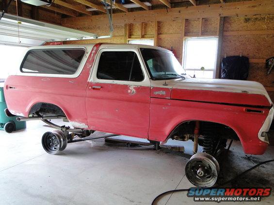1978 Ford Bronco on jack stands, undergoing restoration. Red and white paint, wheels removed