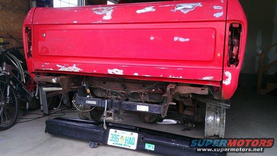 Red pickup truck bed with primer spots, detached bumper, and license plate