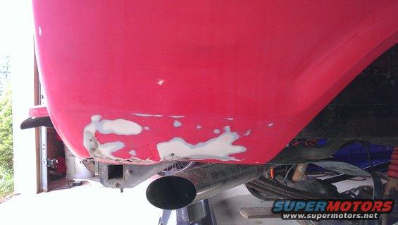 Red vehicle rear quarter panel with body filler and exhaust pipe