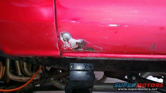 Red vehicle lower body panel with rust and exposed exhaust pipes