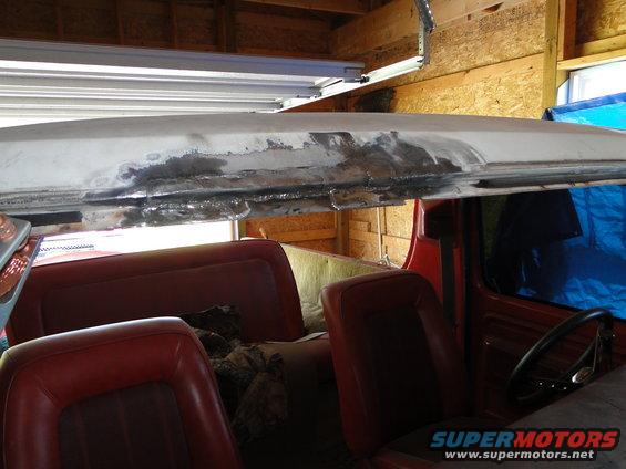 Interior of a red Ford Bronco with red seats, showing the roofline with evidence of bodywork and rust. Steering wheel visible