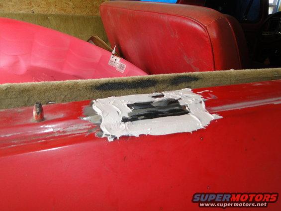 Red car interior showing a damaged body panel with Bondo applied. Red seats are visible in the background