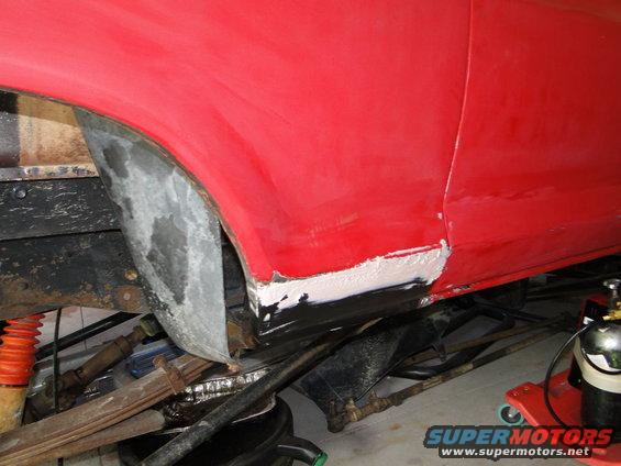 red vehicle body panel with primer and body filler on the lower section near the wheel well