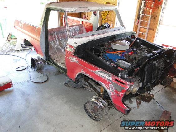 Red and white pickup truck body with engine exposed, missing wheels