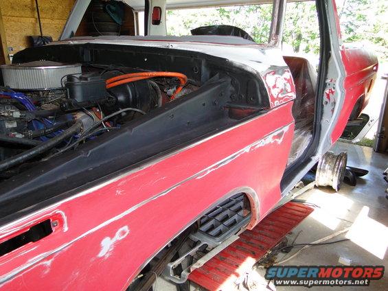 Ford truck body with engine exposed, undergoing restoration. Red paint and primer visible