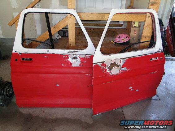 Two red and white car doors with body filler, one open, resting on sawhorses