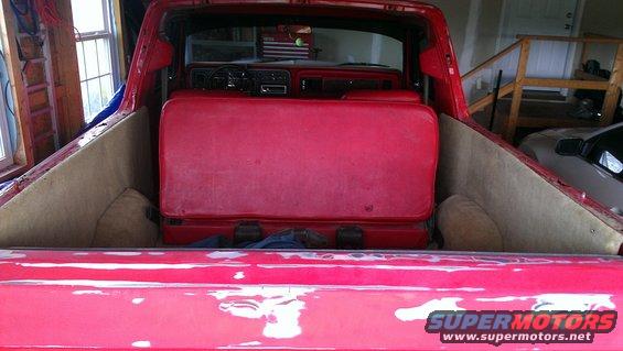 Red 1978 Ford Bronco interior with red seats and tan carpet, viewed from the bed