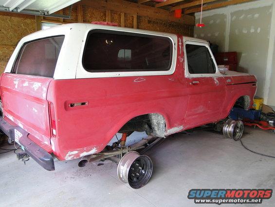 1978 Ford Bronco body, red and white, on jack stands in a garage, undergoing restoration