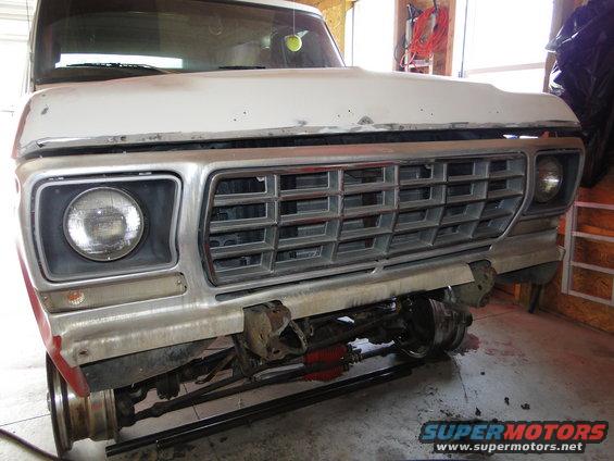 Front view of a white 1970s truck with a large chrome grille and exposed front suspension