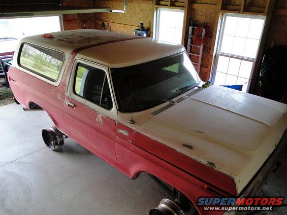 1978 Ford Bronco body in red and white, missing wheels, in a garage