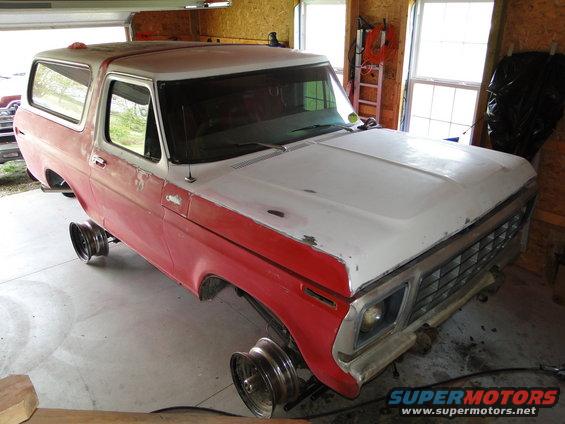 Red and white Ford Bronco on jack stands in a garage, hood is off-white, grille is visible