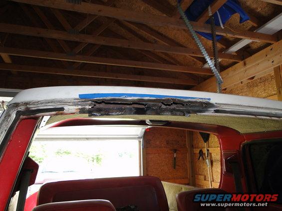 Red 1978 Ford Bronco roof with rust damage and blue tape, viewed from inside