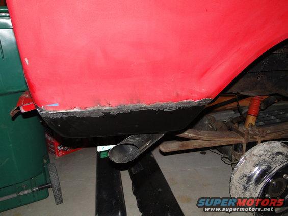 Red vehicle's lower rear quarter panel with exposed metal and exhaust pipe, viewed from below