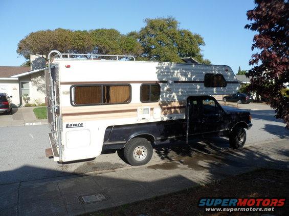 Black pickup truck with a white and tan Lance camper shell, viewed from the side