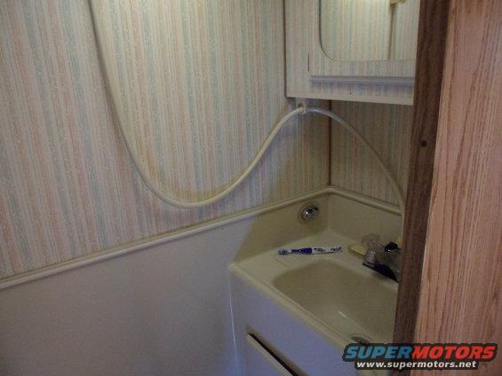 RV bathroom sink with faucet, toothbrush, and shower hose mounted on striped wallpaper