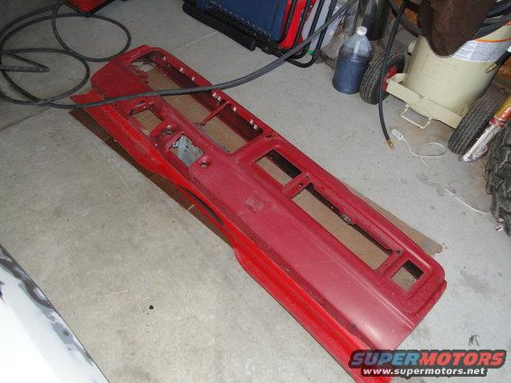 Red dashboard panel with cutouts for gauges and controls, lying on a concrete floor
