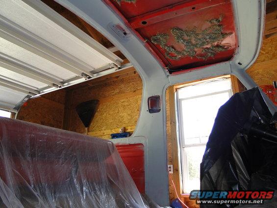 Interior of a 1978 Ford Bronco with red seats covered in plastic, exposed insulation on the roof, and a window