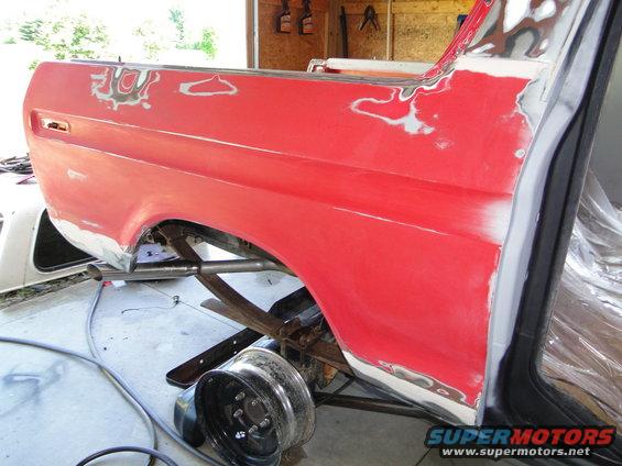 Red vehicle quarter panel and fender being prepped for paint, with a detached wheel nearby