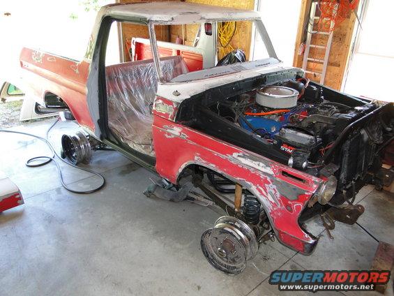Red and white Ford F-Series truck in garage, doors off, engine exposed, undergoing restoration