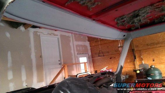 Interior view of a vehicle with red ceiling and exposed insulation, undergoing repairs in a garage